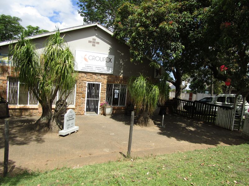 Front exterior view of a commercial office building featuring stone cladding, security gates, and paved frontage with established trees.