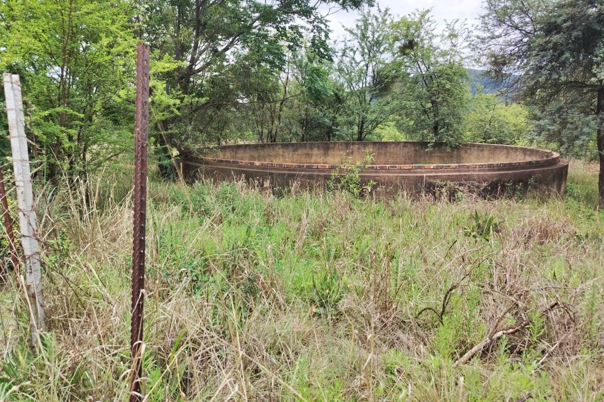 An outdoor area on the farm featuring a large, weathered concrete water reservoir surrounded by overgrown vegetation and a wire fence.