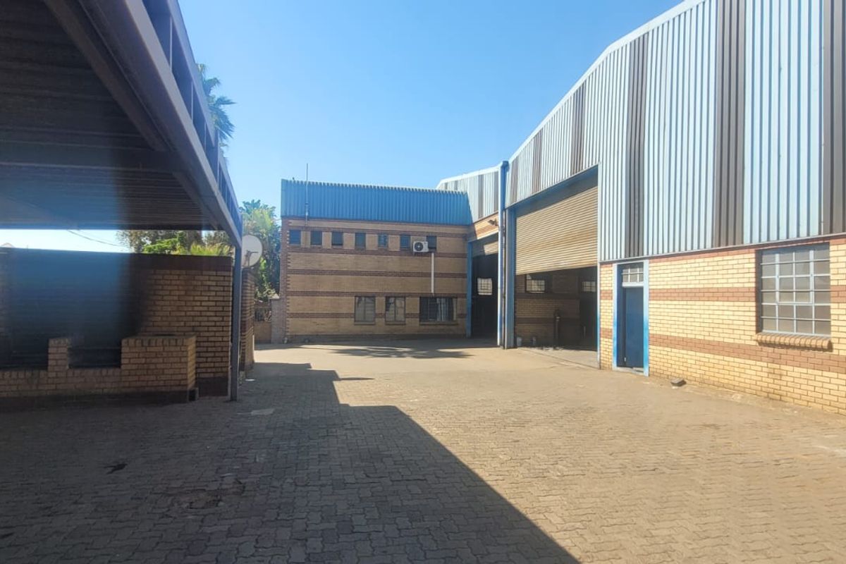 Industrial yard area featuring brick and corrugated metal warehouse buildings, a roller shutter door, and a covered parking structure.