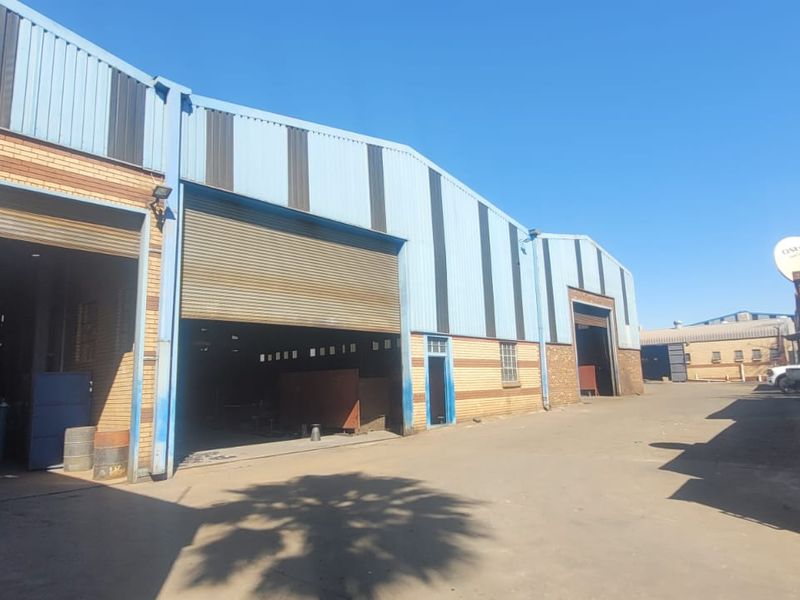 Industrial warehouse facility featuring large roller shutter doors, corrugated metal cladding, and a spacious concrete yard area for vehicle access.