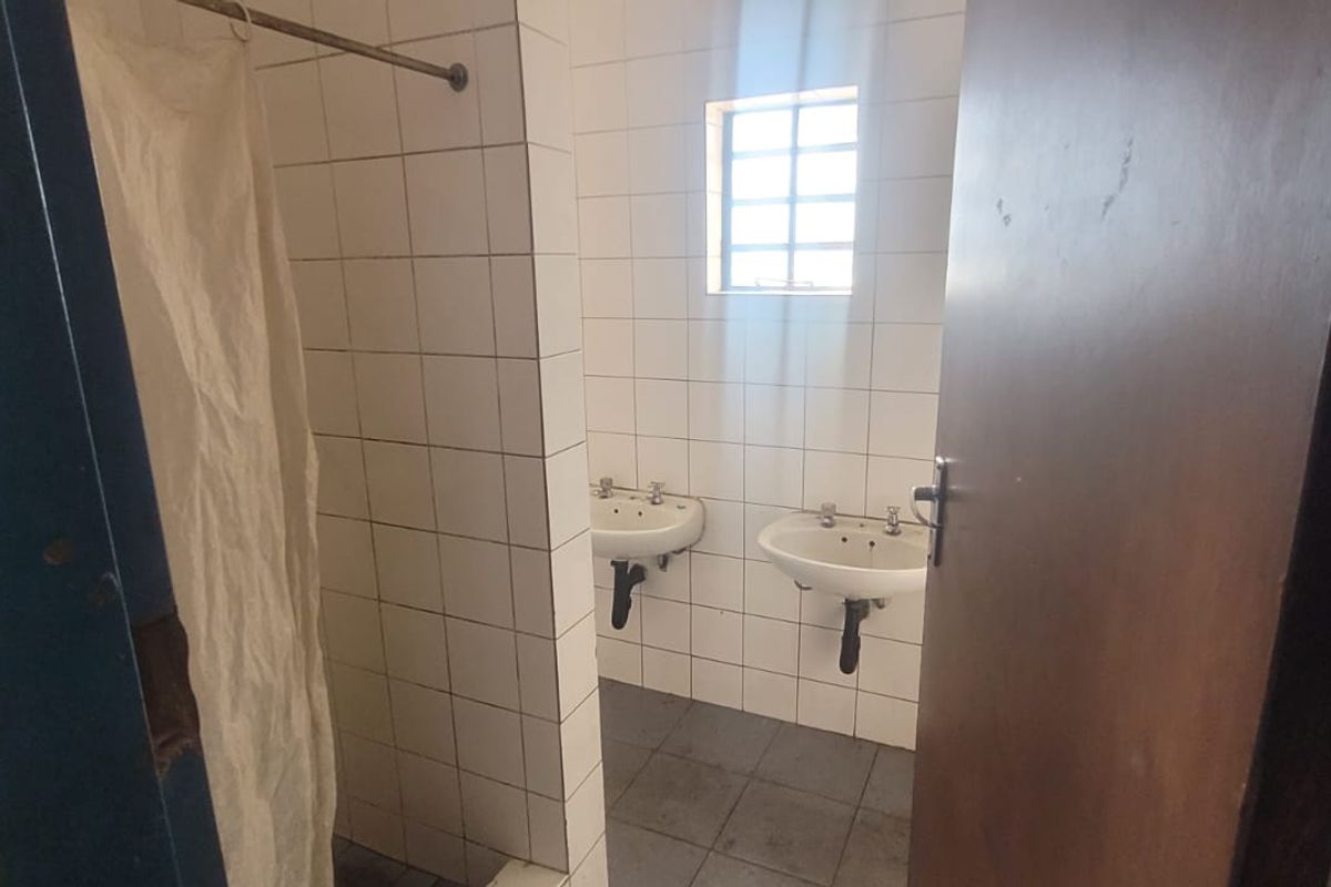 A functional industrial-style bathroom featuring tiled walls and flooring, two wall-mounted basins, and a shower area.