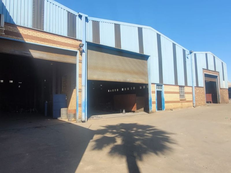 Industrial warehouse facility featuring multiple large roller shutter doors, brick and metal cladding construction, and a spacious concrete yard area.