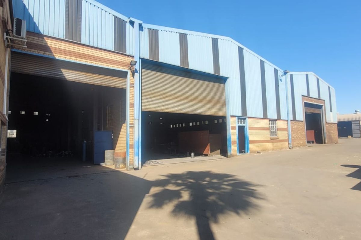 Industrial warehouse facility featuring multiple large roller shutter doors, brick and metal cladding construction, and a spacious concrete yard area.