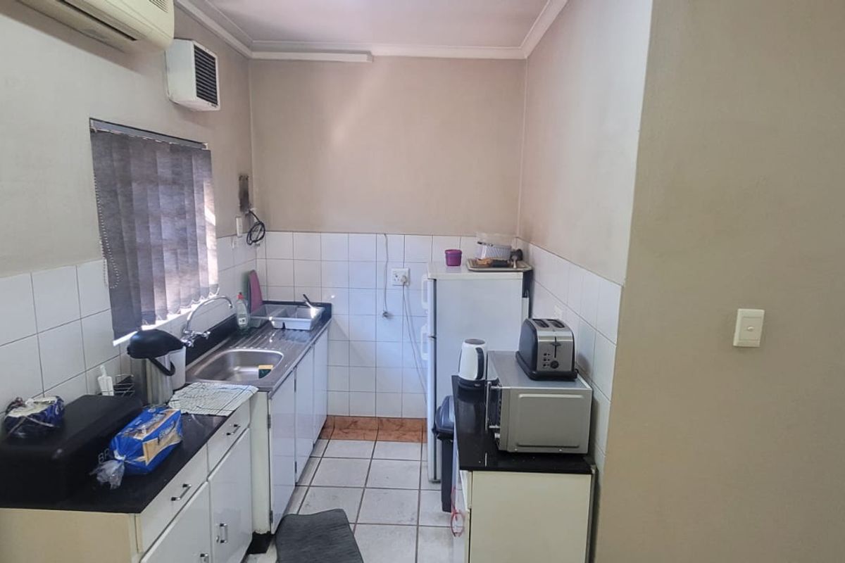 Compact kitchen area featuring built-in cabinetry, tiled backsplash, stainless steel sink, and wall-mounted air conditioning unit within an industrial property setting.