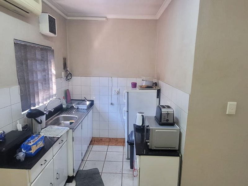 Compact kitchen area featuring built-in cabinetry, tiled backsplash, stainless steel sink, and wall-mounted air conditioning unit within an industrial property setting.
