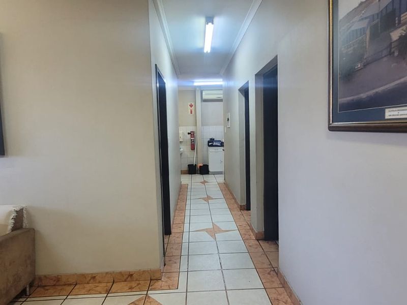 A functional industrial hallway featuring ceramic tiled flooring and overhead fluorescent lighting, providing access to multiple rooms.
