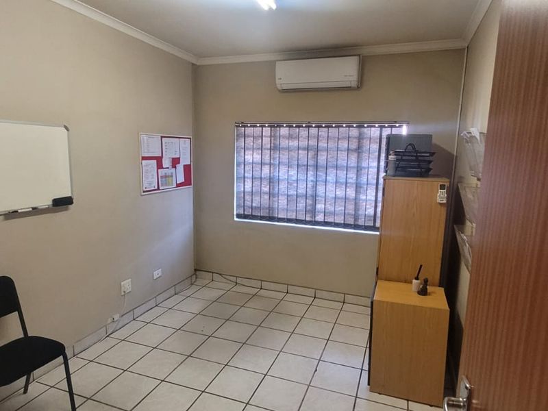A functional office space featuring tiled flooring, a wall-mounted split-system air conditioner, and window blinds.
