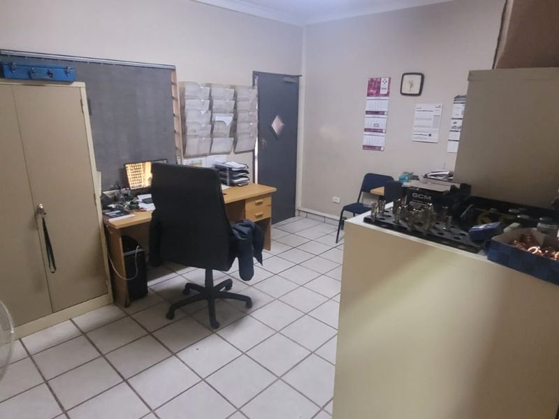 A functional industrial office space featuring tiled flooring and a secure metal door, suitable for administrative or operational use.