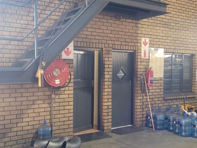 Industrial utility area featuring exposed brick walls, a steel staircase, and essential fire safety equipment including a hose reel and extinguisher.
