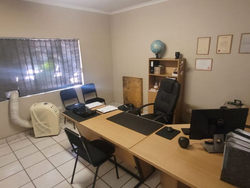 A functional office space featuring tiled flooring and vertical window blinds, suitable for a professional work environment.