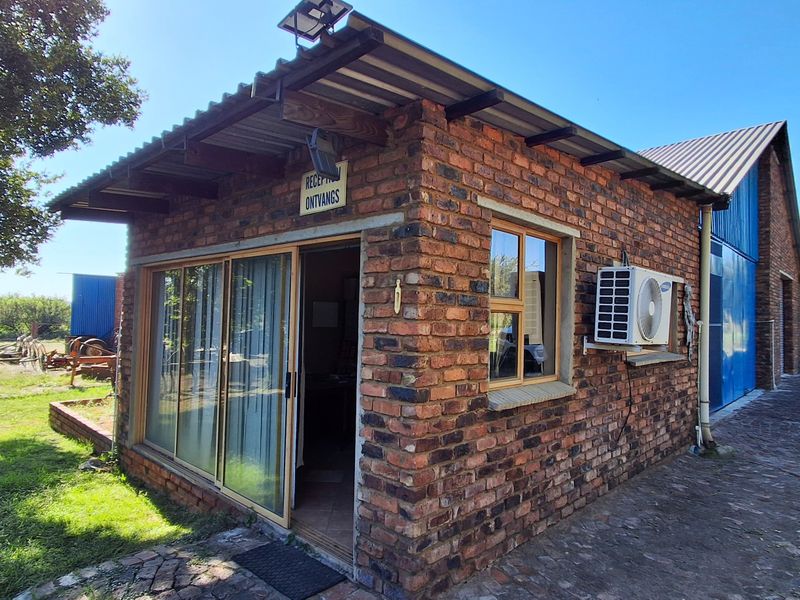 Exterior view of a rustic brick farm building featuring a sliding glass entrance, external air conditioning unit, and a corrugated metal roof.