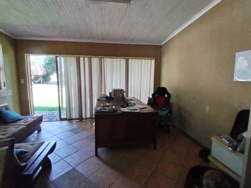 A functional home office space featuring tiled flooring, a timber ceiling, and large sliding glass doors providing direct access to the garden.