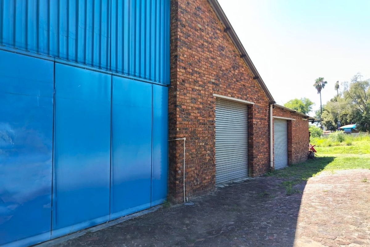 Exterior view of a farm outbuilding featuring brick construction, corrugated metal siding, and multiple roller shutter doors.