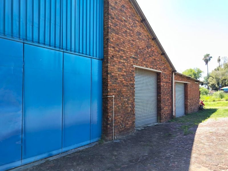 Exterior view of a farm outbuilding featuring brick construction, corrugated metal siding, and multiple roller shutter doors.