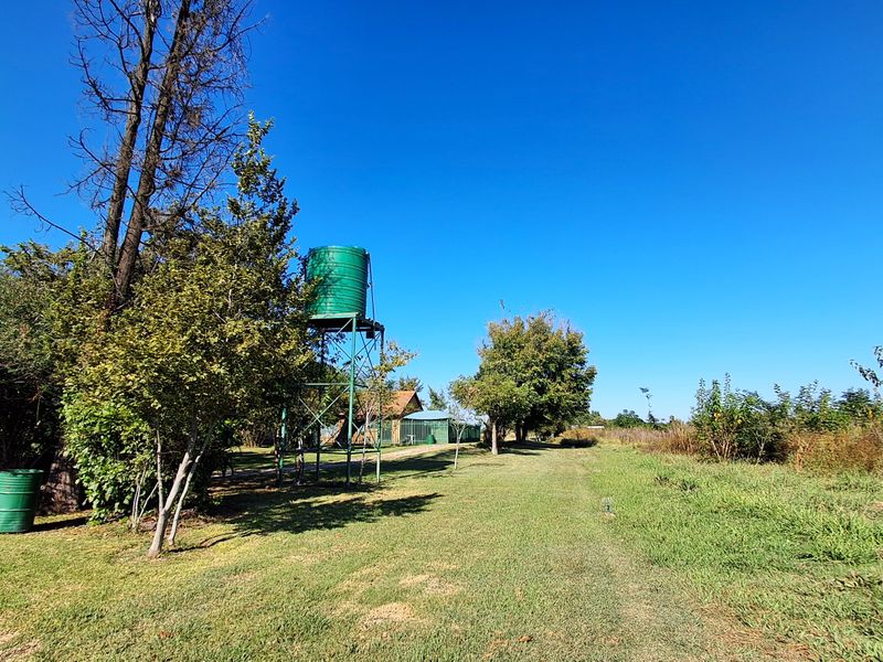 A spacious farm garden area featuring an elevated water storage tank on a metal support structure set within a well-maintained grassy landscape.