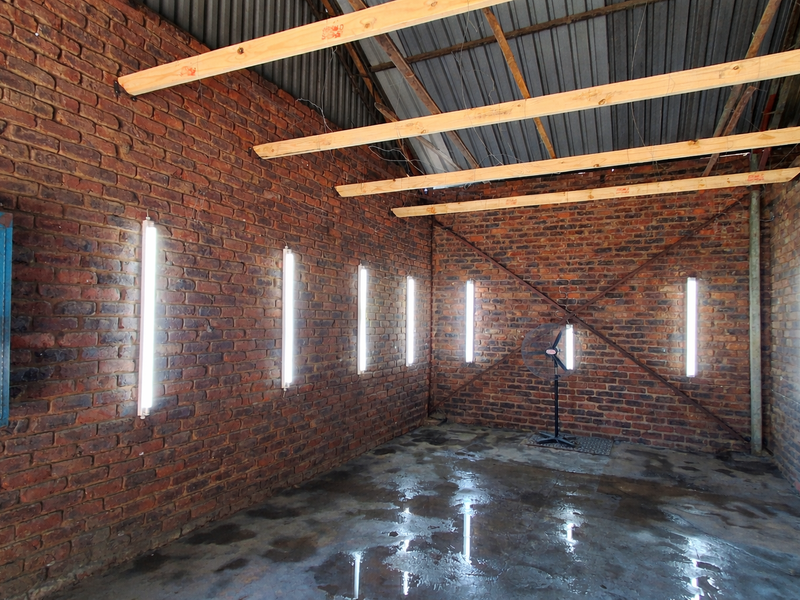 A utilitarian space featuring exposed brick walls, concrete flooring, and industrial-style fluorescent lighting, suitable for a workshop or storage area.