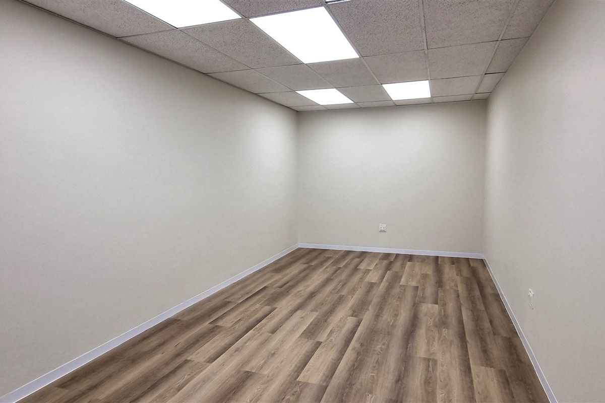 A clean, vacant office space featuring modern laminate wood flooring, neutral walls, and a drop ceiling with integrated LED panel lighting.
