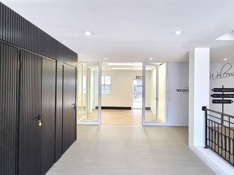 Modern office lobby area featuring sleek slatted wall paneling, glass partition doors, and a contemporary metal balustrade overlooking the lower level.