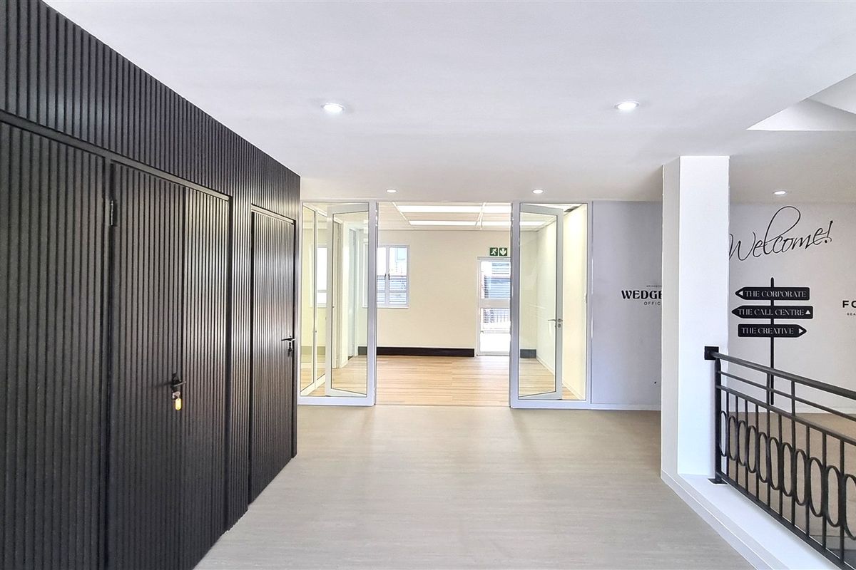 Modern office lobby area featuring sleek slatted wall paneling, glass partition doors, and a contemporary metal balustrade overlooking the lower level.