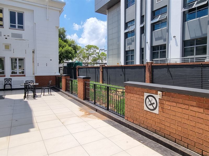A paved outdoor patio area featuring brick boundary walls with electric fencing, adjacent to the office building structure.