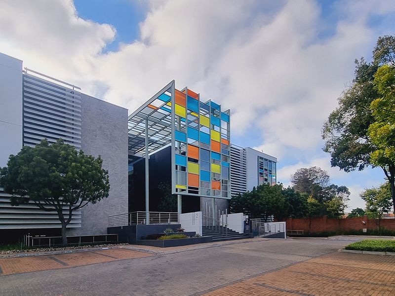 Modern office building exterior featuring a distinctive colorful facade, metal louvers, and a paved entrance area with professional landscaping.
