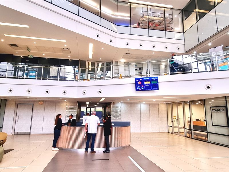 Modern office building lobby featuring a central reception desk, multi-level atrium design, glass partitions, and high-quality tiled flooring.