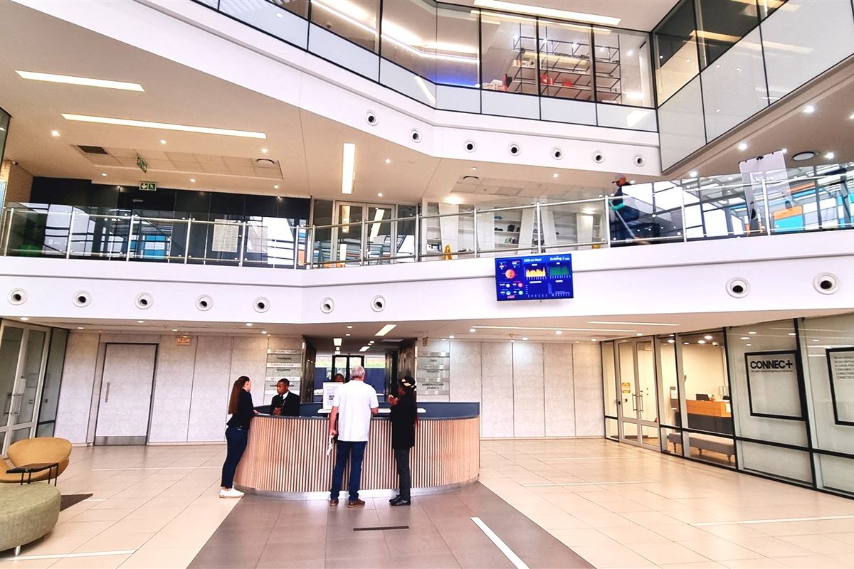 Modern office building lobby featuring a central reception desk, multi-level atrium design, glass partitions, and high-quality tiled flooring.