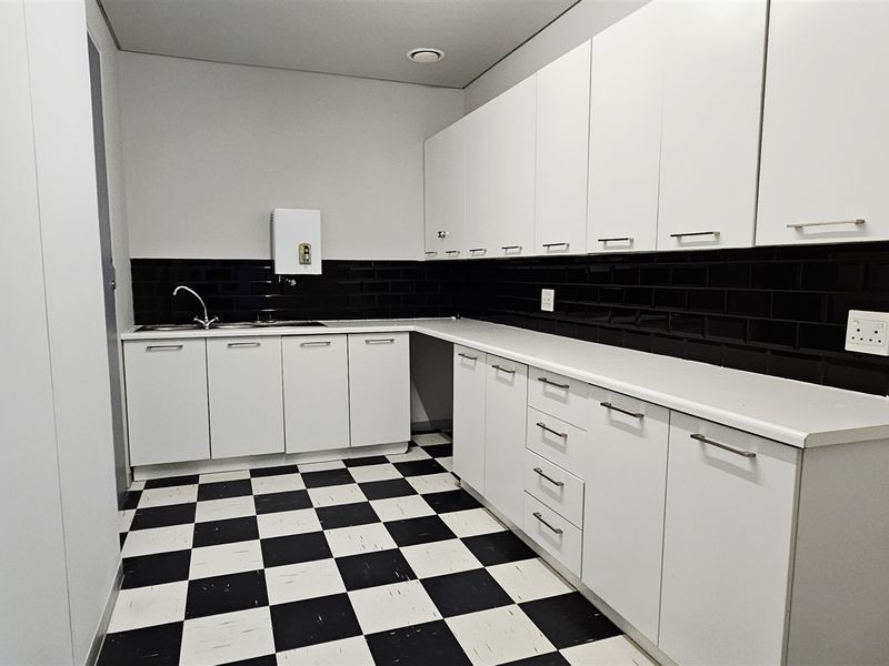 A clean, functional office kitchenette featuring white cabinetry, a black subway tile backsplash, and distinctive checkerboard flooring.