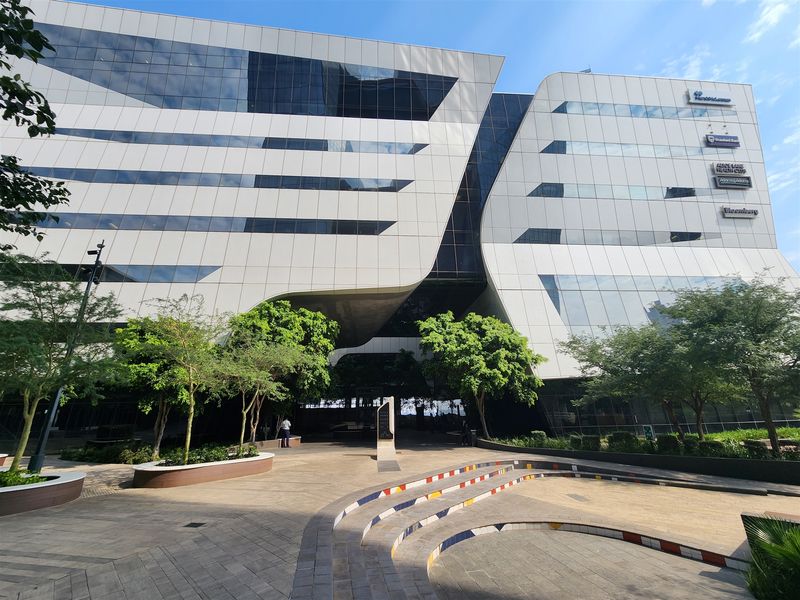 Modern commercial office building featuring a striking glass and composite panel facade with a landscaped pedestrian plaza and stepped seating area.