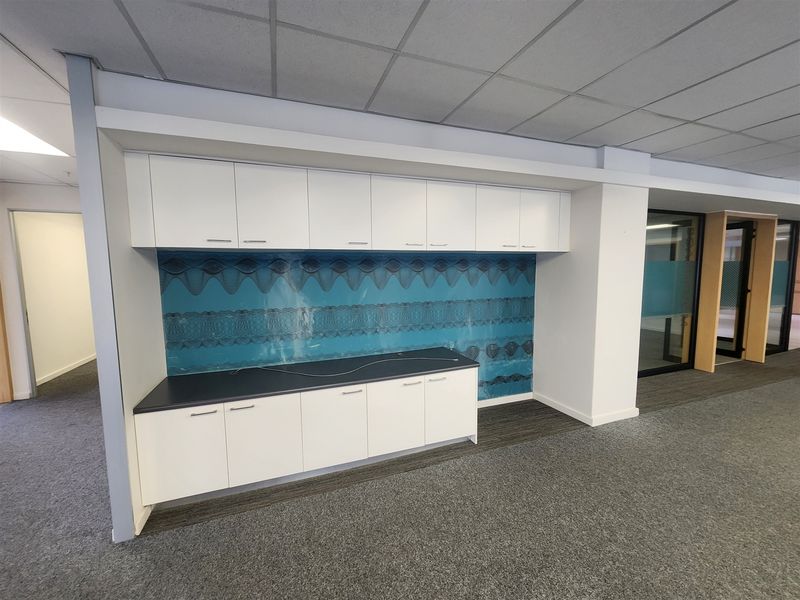 A modern office space featuring built-in white cabinetry with a decorative blue backsplash, suspended ceiling, and neutral carpet flooring.