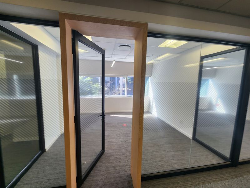 A bright, empty office space featuring modern glass partitions, timber door frames, and professional carpet flooring, ideal for a corporate workspace.