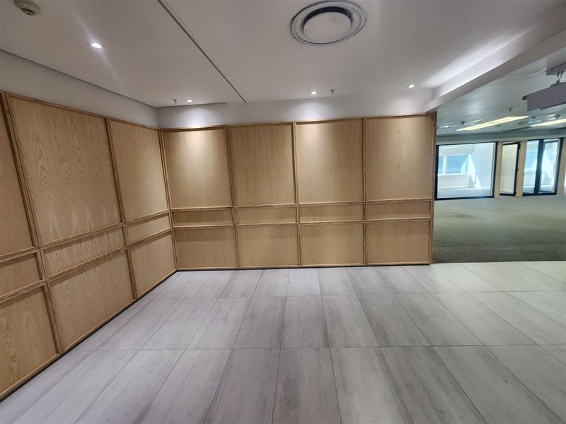 A bright, empty office space featuring modern wood wall paneling, recessed ceiling lighting, and neutral tiled flooring, offering a clean professional environment.