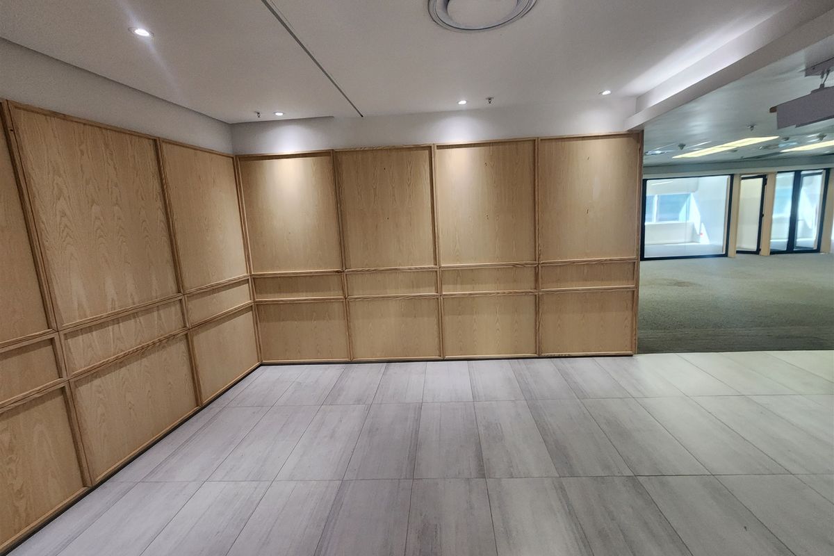 A bright, empty office space featuring modern wood wall paneling, recessed ceiling lighting, and neutral tiled flooring, offering a clean professional environment.
