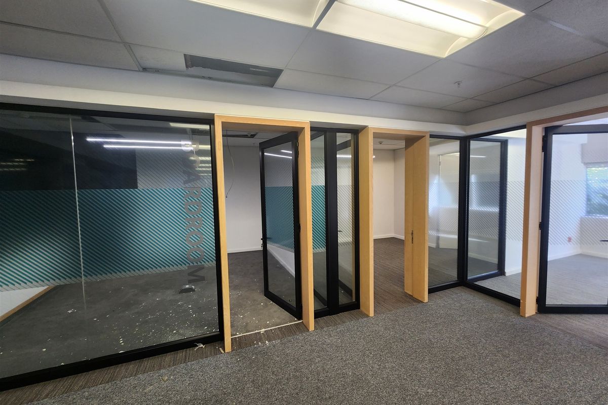 Empty office space featuring modern glass partitions with timber frames, carpeted flooring, and a suspended ceiling with integrated lighting.