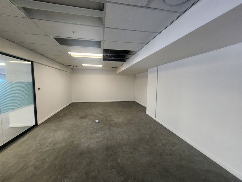 An empty office space featuring a suspended ceiling with fluorescent lighting, carpet flooring, and a glass partition wall.