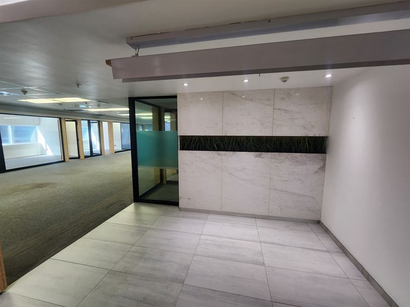 A modern office reception area featuring marble-look wall cladding, recessed lighting, and a glass partition door, leading into an open-plan workspace.