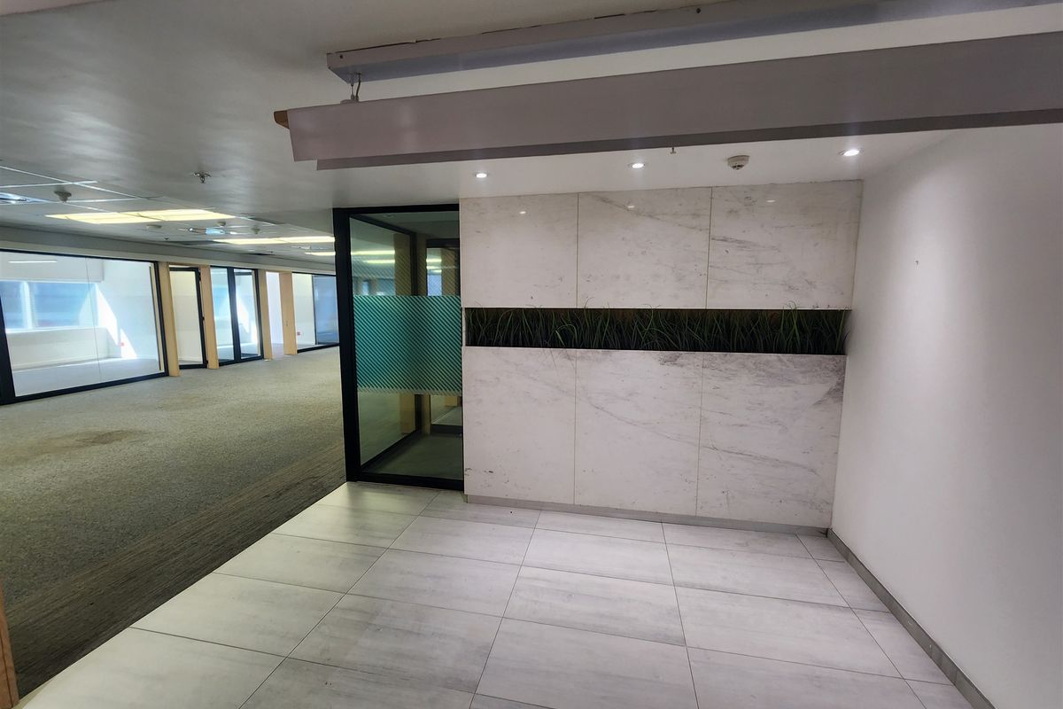 A modern office reception area featuring marble-look wall cladding, recessed lighting, and a glass partition door, leading into an open-plan workspace.