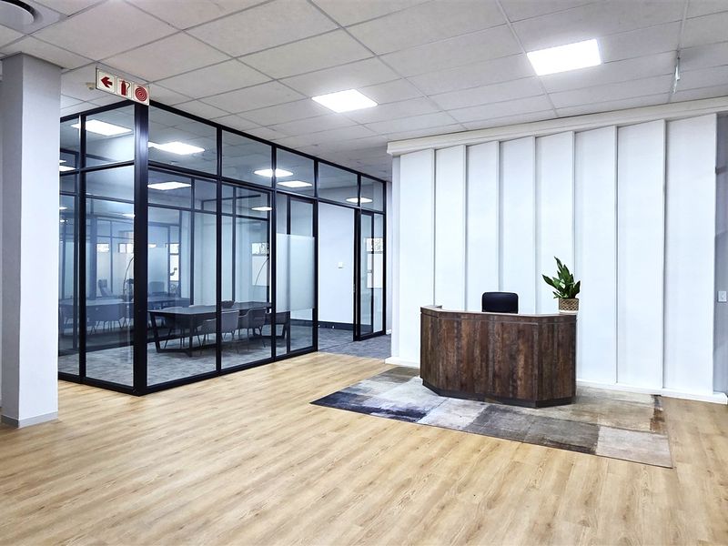 Modern office reception area featuring glass-partitioned meeting rooms, sleek laminate flooring, and professional recessed lighting in a contemporary open-plan layout.