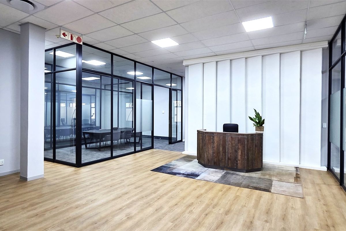 Modern office reception area featuring glass-partitioned meeting rooms, sleek laminate flooring, and professional recessed lighting in a contemporary open-plan layout.