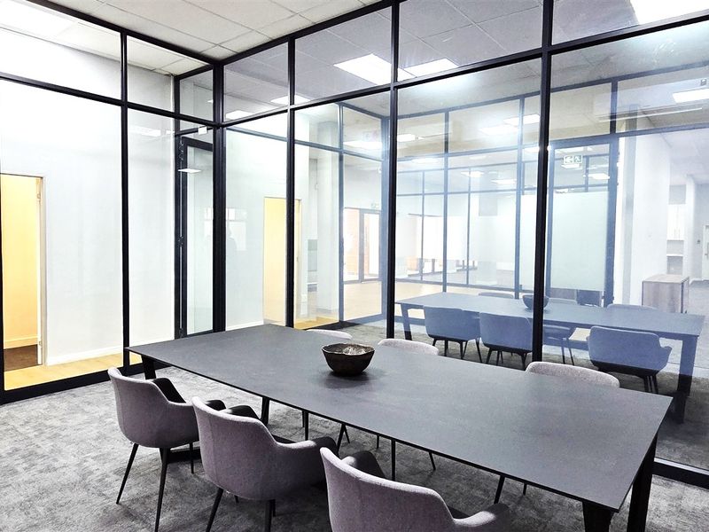 Modern office meeting room featuring sleek black aluminum framed glass partitions, recessed ceiling lighting, and professional carpeted flooring.