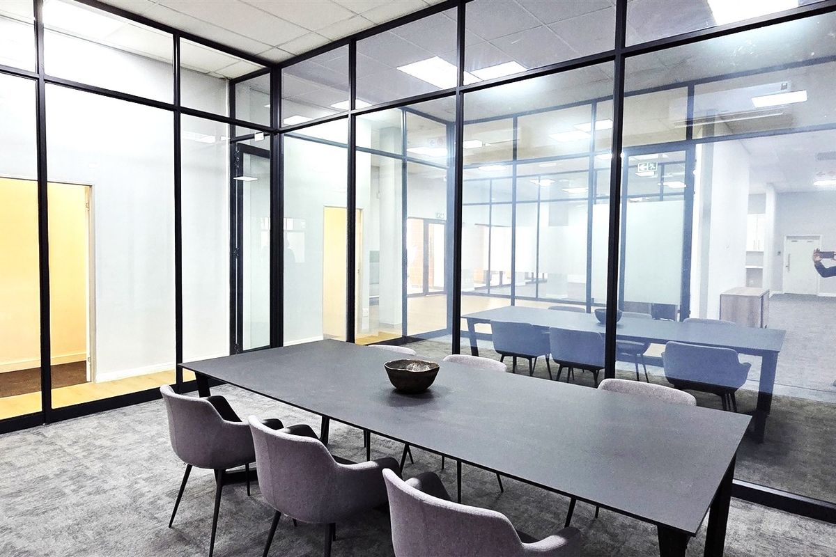 Modern office meeting room featuring sleek black aluminum framed glass partitions, recessed ceiling lighting, and professional carpeted flooring.
