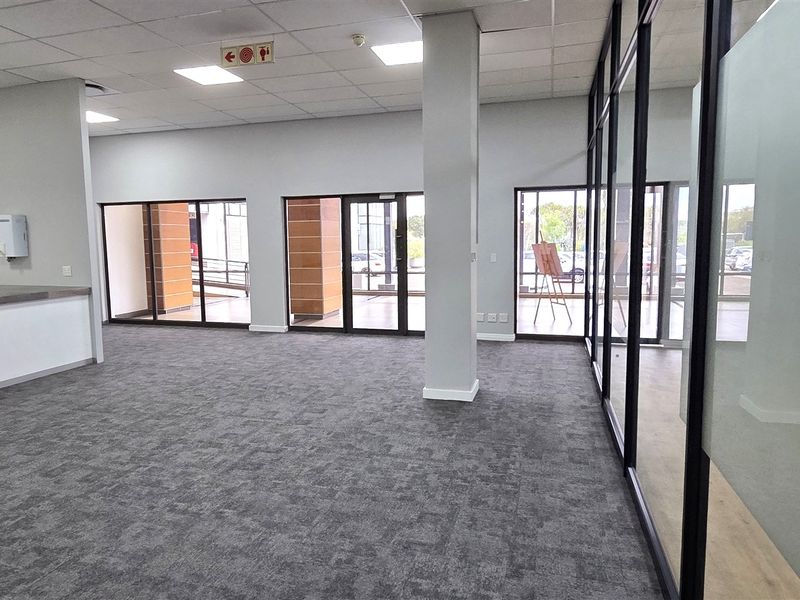 Spacious open-plan office area featuring modern glass partitions, carpeted flooring, recessed lighting, and a convenient built-in kitchenette counter.