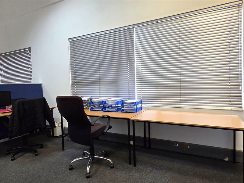 A functional office space featuring large windows with venetian blinds, carpeted flooring, and wall-mounted fire safety equipment.
