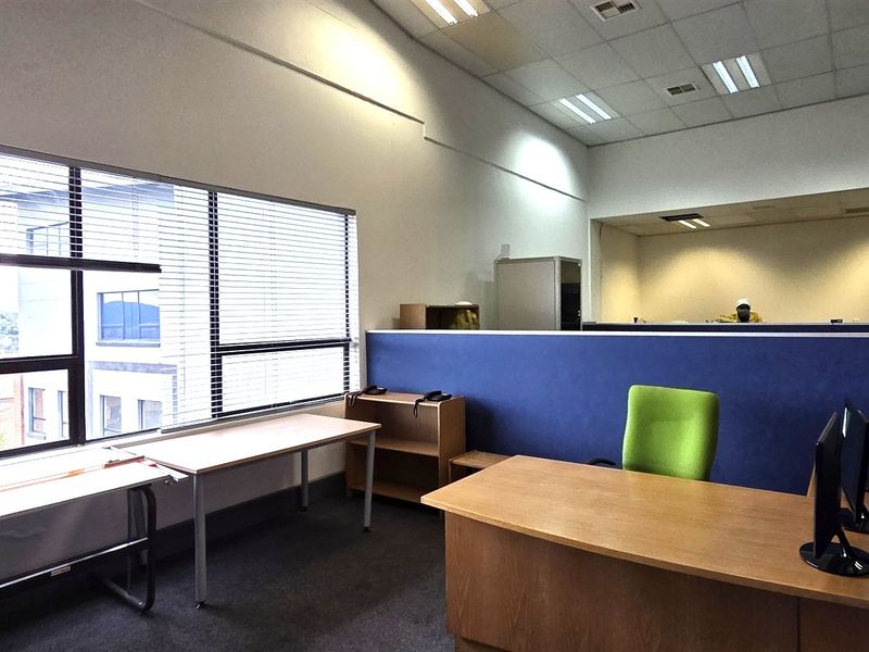 Open-plan office space featuring large windows with venetian blinds, suspended ceilings, and blue partition walls, offering a functional workspace environment.