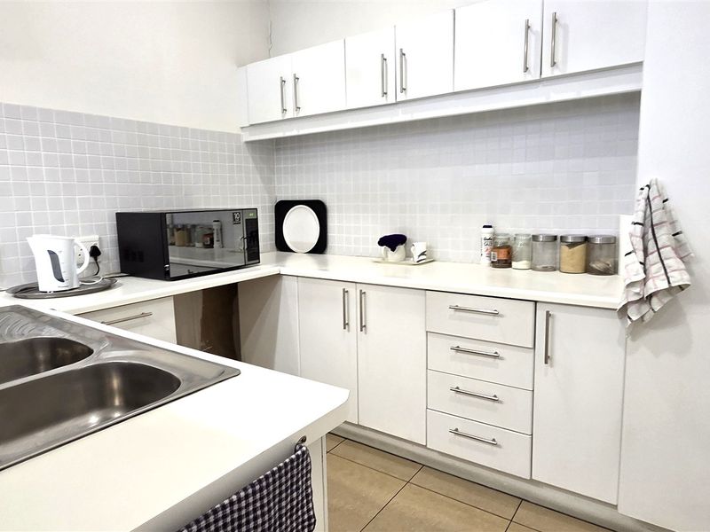 A functional office kitchen featuring white cabinetry, laminate countertops, a double bowl stainless steel sink, and a tiled backsplash.