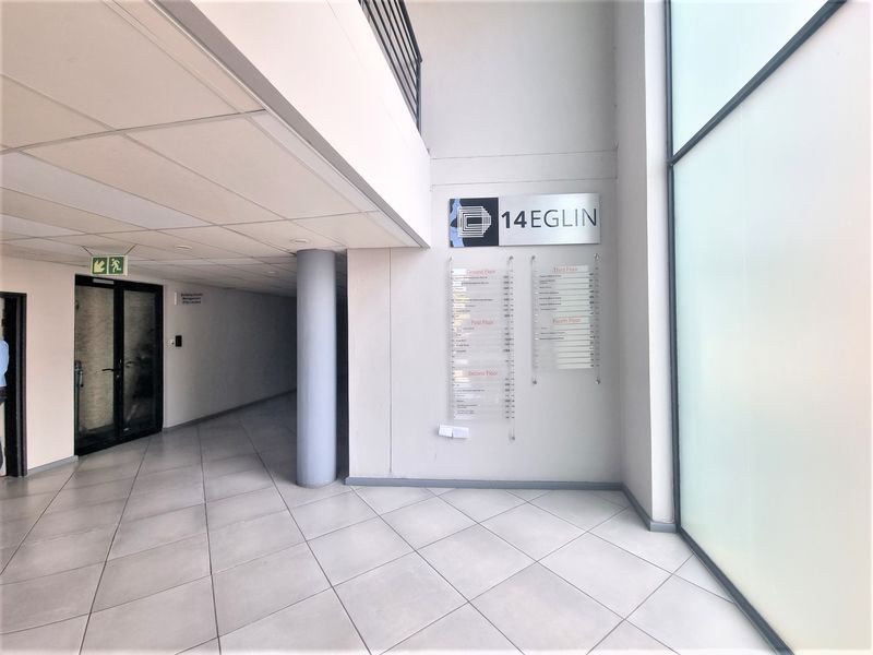 A bright and modern office building entrance lobby featuring tiled flooring, a directory board, and a double-volume ceiling.