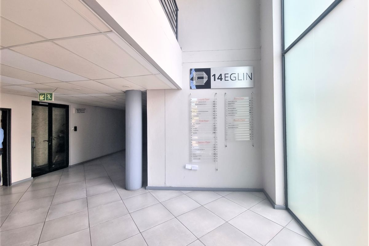 A bright and modern office building entrance lobby featuring tiled flooring, a directory board, and a double-volume ceiling.