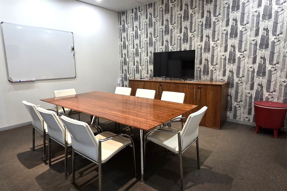 A functional office meeting room featuring a large conference table, wall-mounted whiteboard, and patterned feature wall.