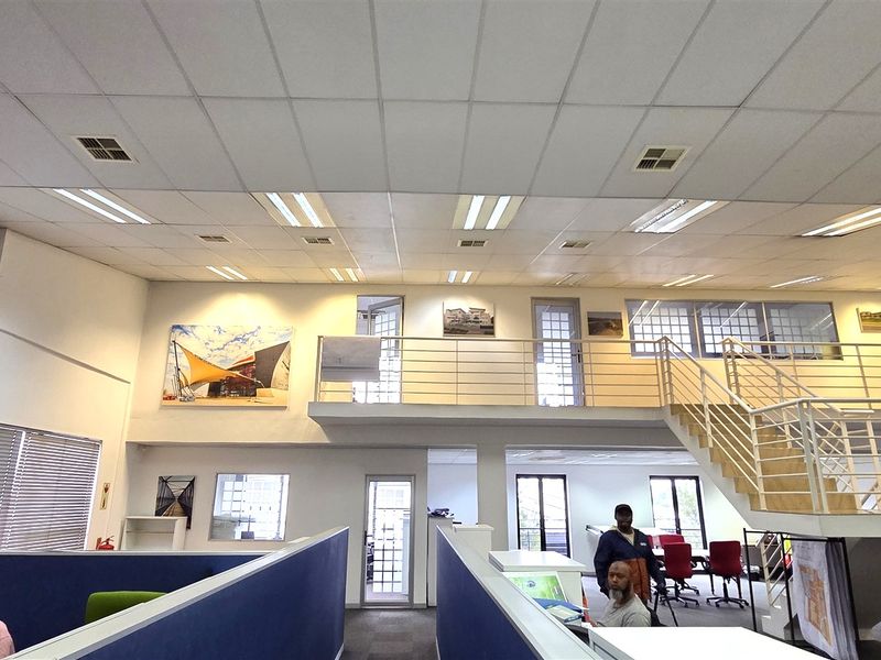 Spacious open-plan office area featuring a mezzanine level, metal staircase, and suspended ceiling with integrated lighting.