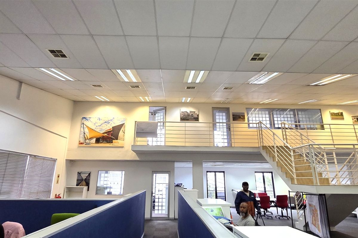 Spacious open-plan office area featuring a mezzanine level, metal staircase, and suspended ceiling with integrated lighting.